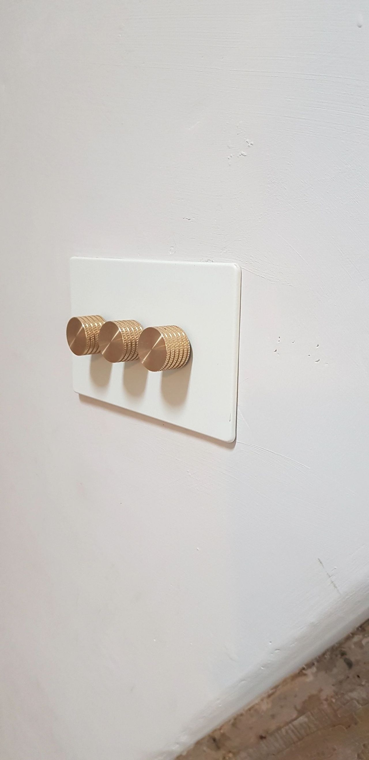 Triple brass rotary dimmer switch on a white plate